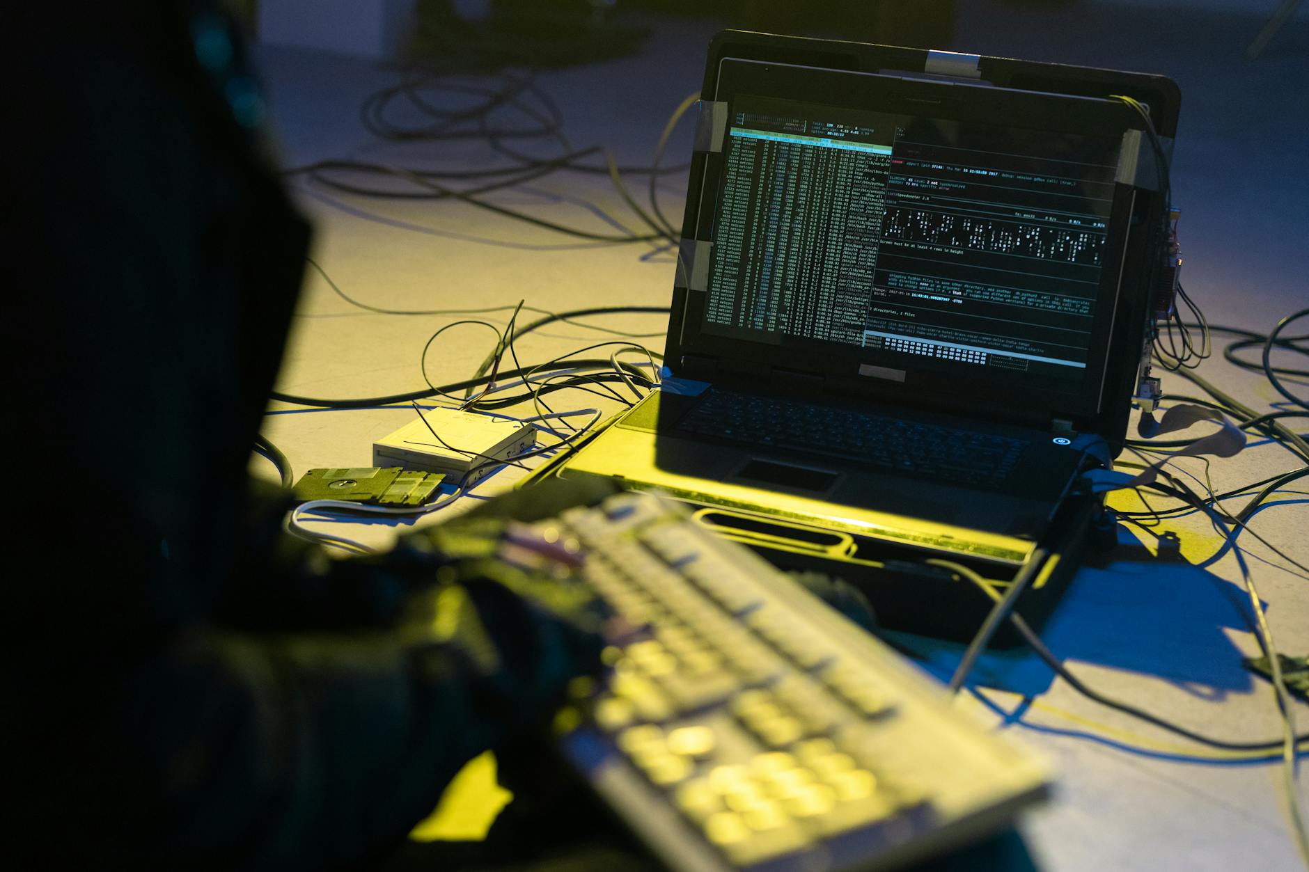 Osoba pisząca kod na laptopie otoczonym kablami