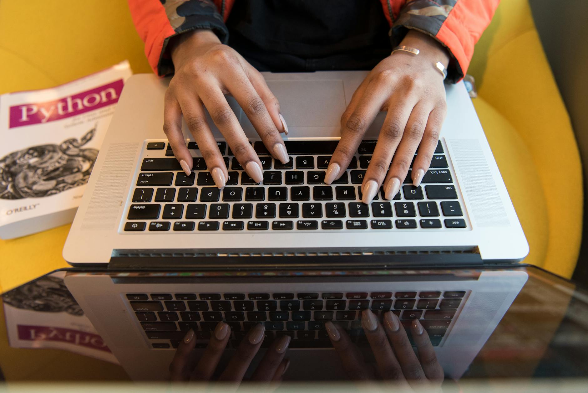 Osoba pisząca na laptopie obok książki o programowaniu w Pythonie