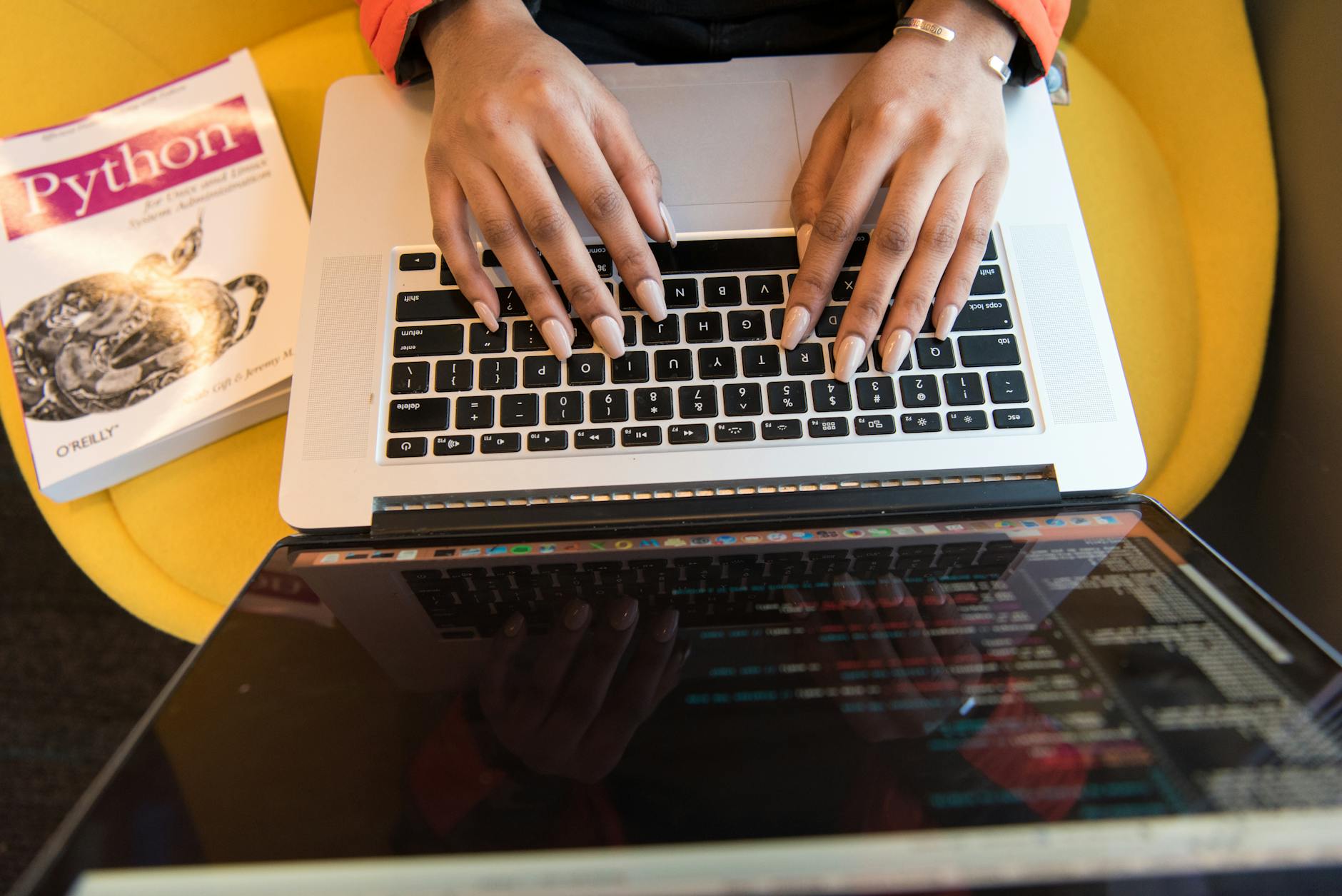 Programista piszący kod Pythona na laptopie obok książki o Pythonie