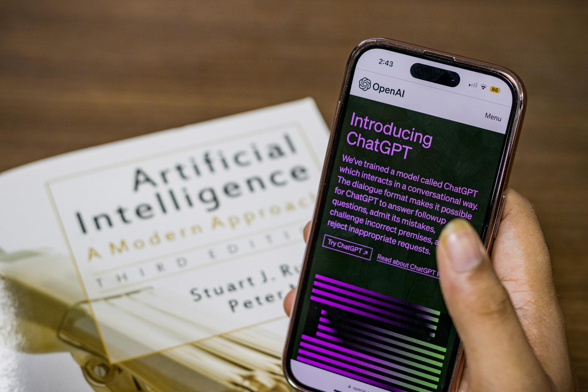 Smartfon z aplikacją ChatGPT trzymany nad podręcznikiem o sztucznej inteligencji